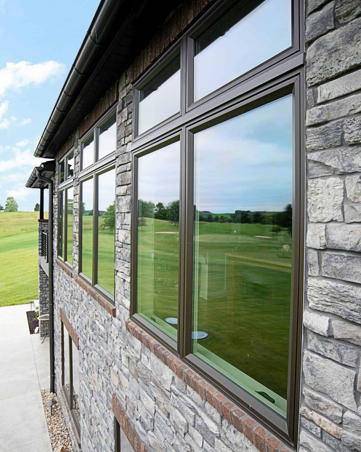 A modern building in St. Louis with large, dark-framed casement windows reflects a grassy landscape and sky. The exterior features textured stone, complemented by a concrete path and green lawn on a clear day.